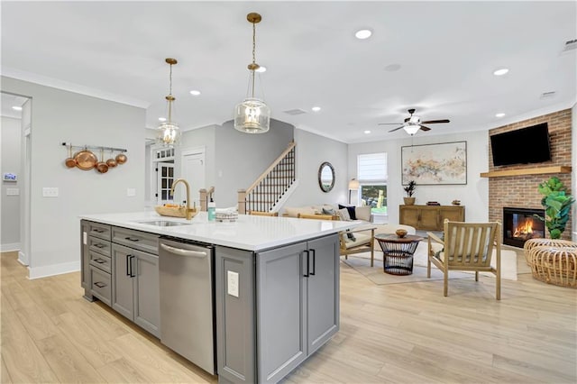 kitchen with sink, dishwasher, gray cabinetry, hanging light fixtures, and a center island with sink