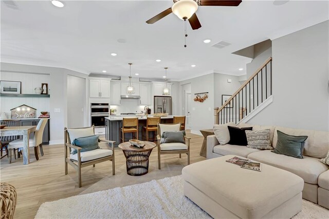 living room featuring ceiling fan, a brick fireplace, ornamental molding, and light hardwood / wood-style floors