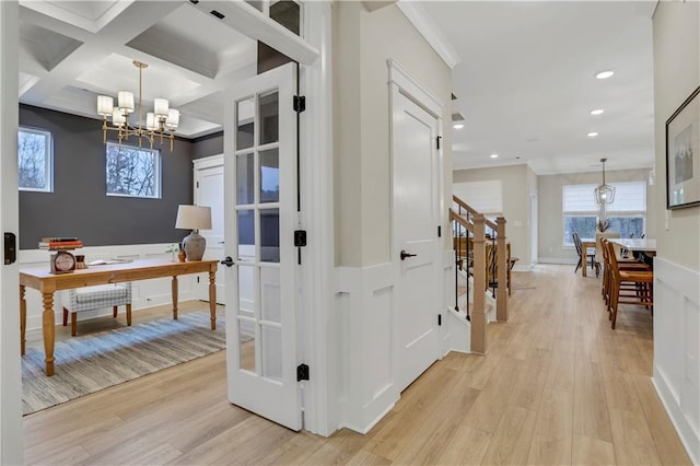 corridor with beam ceiling, coffered ceiling, a chandelier, and light wood-type flooring