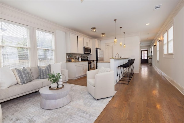 living area with wood finished floors, visible vents, baseboards, recessed lighting, and crown molding