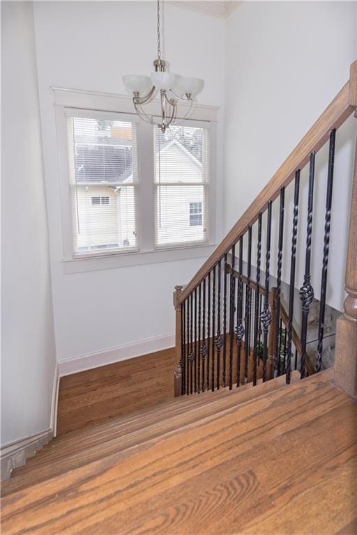 stairway featuring a chandelier, baseboards, and wood finished floors