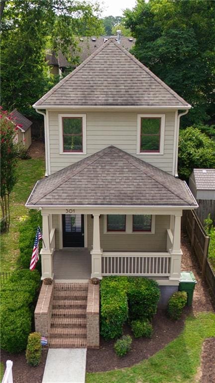 view of front of house with roof with shingles, a porch, and fence