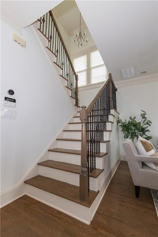 stairway with crown molding, wood finished floors, baseboards, and a chandelier