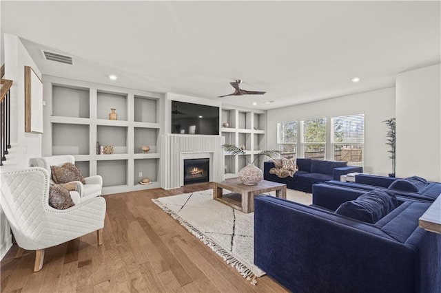 living room featuring built in shelves, ceiling fan, and wood-type flooring