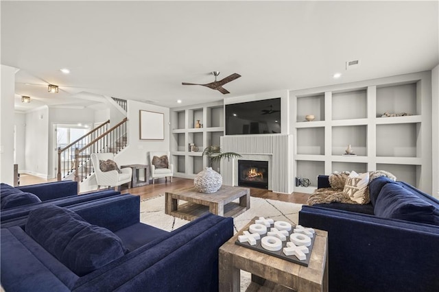 living room featuring wood-type flooring, built in features, and ceiling fan