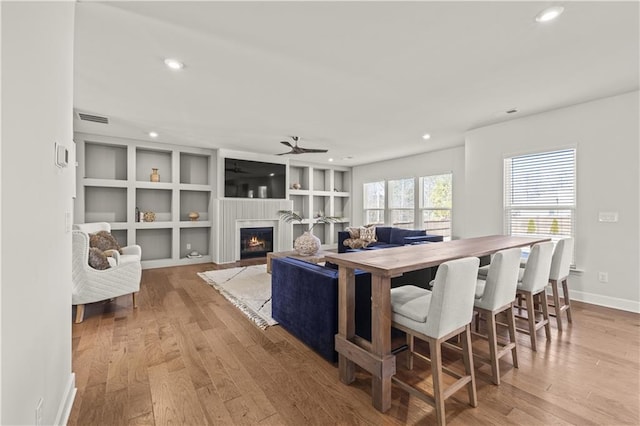 living room with built in shelves, ceiling fan, and light wood-type flooring