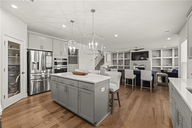 kitchen featuring gray cabinets, appliances with stainless steel finishes, hardwood / wood-style floors, hanging light fixtures, and a center island