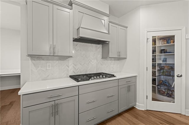 kitchen featuring gray cabinetry, custom range hood, wood-type flooring, and stainless steel gas cooktop