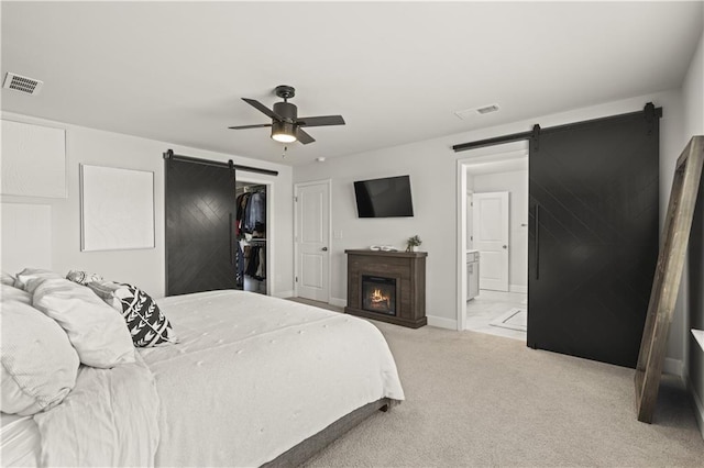 carpeted bedroom featuring a walk in closet, a barn door, a closet, and ensuite bath