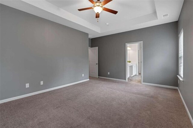 unfurnished bedroom with ceiling fan, a raised ceiling, connected bathroom, and light carpet