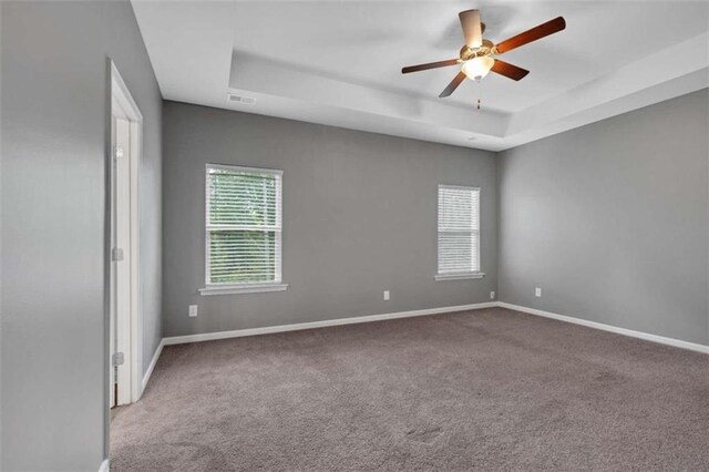 empty room with ceiling fan, a raised ceiling, and carpet flooring