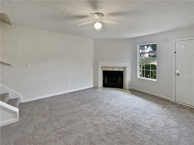 unfurnished living room with ceiling fan, a textured ceiling, light carpet, and a tile fireplace