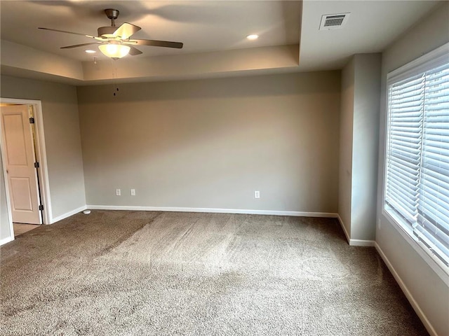 spare room featuring baseboards, visible vents, a ceiling fan, carpet, and a tray ceiling