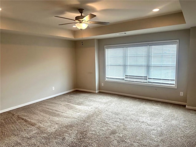 carpeted empty room featuring ceiling fan, a raised ceiling, visible vents, and baseboards