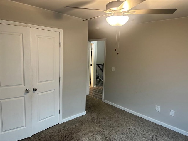 unfurnished bedroom with ceiling fan, dark colored carpet, a closet, and baseboards