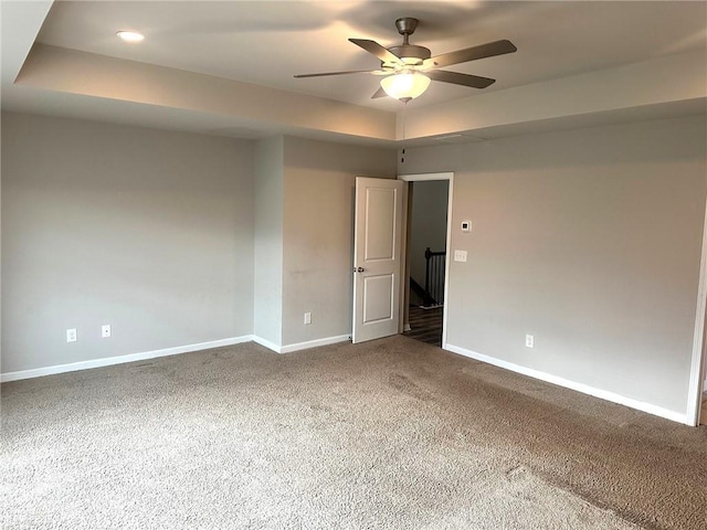 carpeted empty room with ceiling fan, baseboards, and a raised ceiling