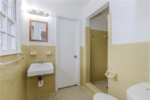 bathroom with tiled shower, toilet, sink, and tile walls