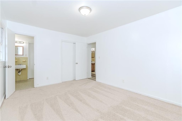 unfurnished bedroom with a closet, connected bathroom, sink, and light carpet