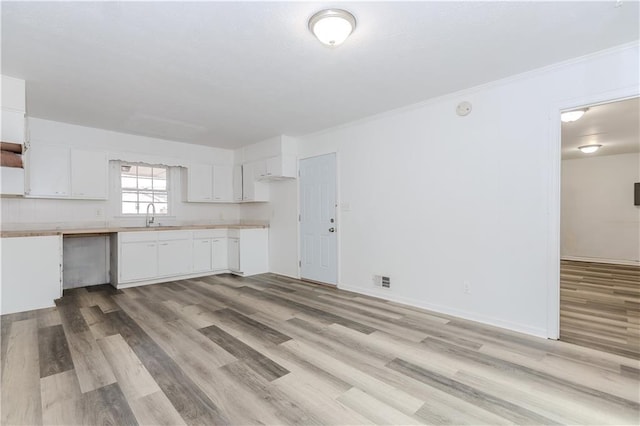 kitchen with white cabinetry, crown molding, sink, and light wood-type flooring