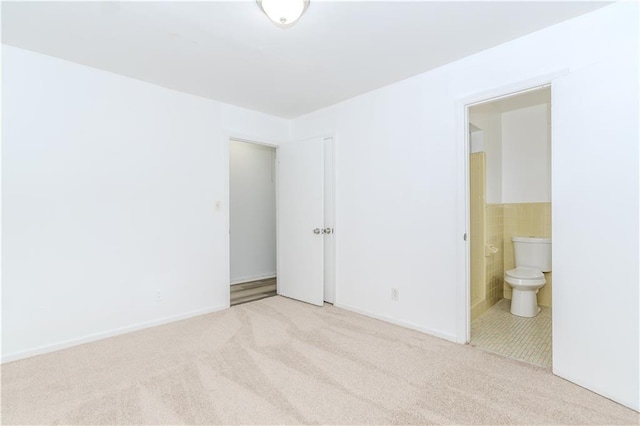 unfurnished bedroom featuring ensuite bath, light carpet, and tile walls