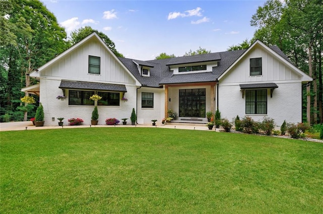 modern farmhouse with brick siding, a shingled roof, and a front lawn