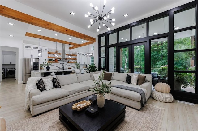 living area with light wood-style floors, beamed ceiling, separate washer and dryer, and a notable chandelier