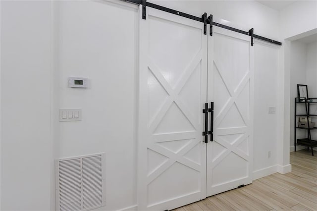 interior space featuring a barn door, wood finished floors, visible vents, and baseboards