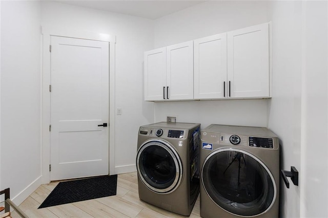 clothes washing area featuring separate washer and dryer, cabinet space, light wood-style floors, and baseboards