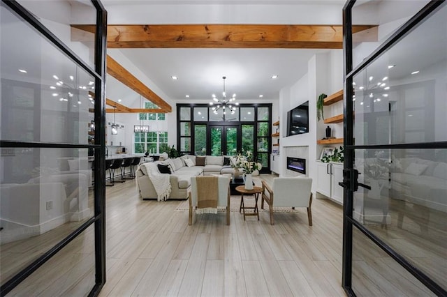 living area with a chandelier, beamed ceiling, light wood-type flooring, french doors, and a glass covered fireplace