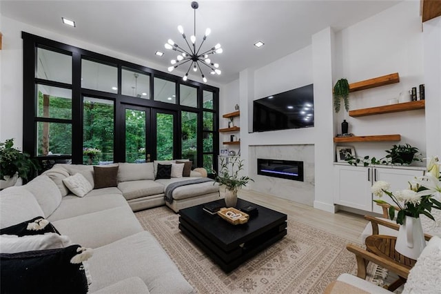 living area featuring a chandelier, french doors, light wood-style floors, and a premium fireplace