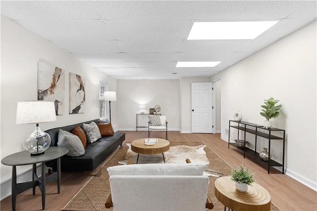 living room featuring light wood finished floors, baseboards, and a drop ceiling