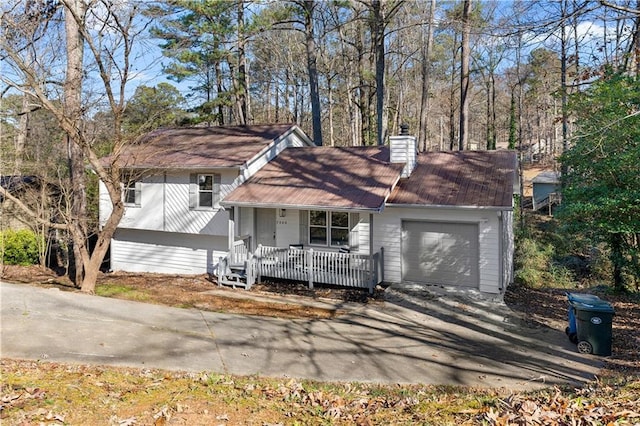 split level home with a garage, driveway, a chimney, and covered porch