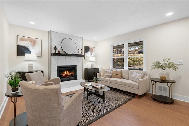 living room featuring wood finished floors, a fireplace, baseboards, visible vents, and recessed lighting