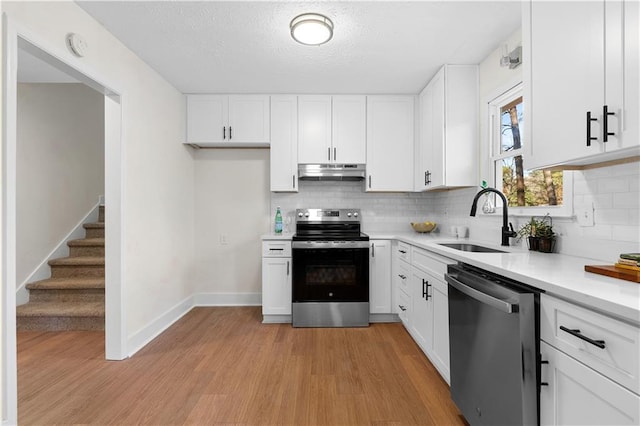 kitchen with a sink, decorative backsplash, appliances with stainless steel finishes, light countertops, and under cabinet range hood