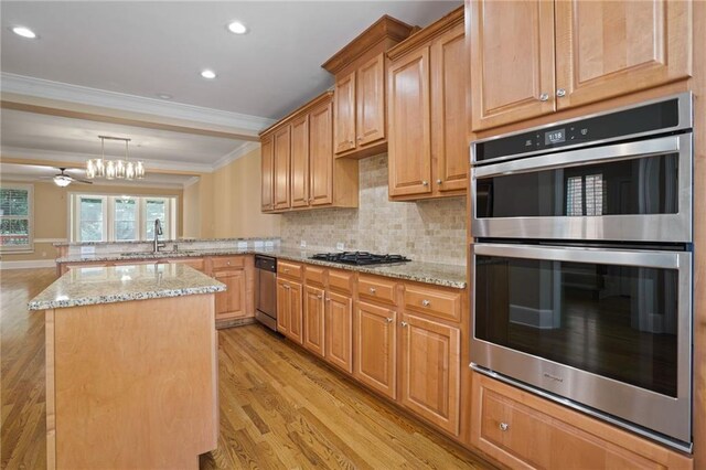 kitchen with appliances with stainless steel finishes, kitchen peninsula, light hardwood / wood-style flooring, ornamental molding, and sink