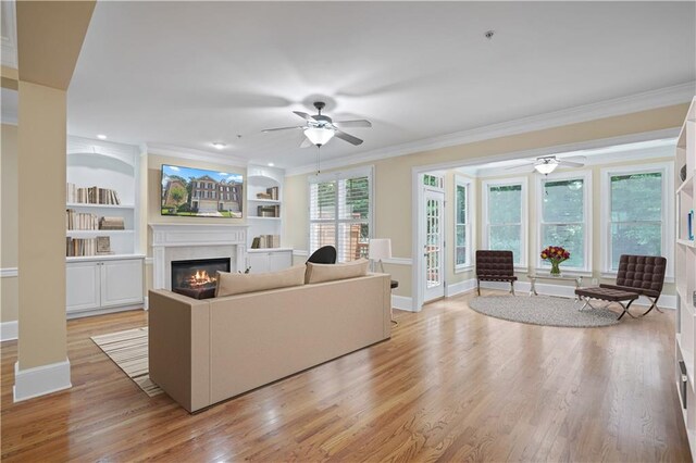 living room with crown molding, ceiling fan, light hardwood / wood-style flooring, built in shelves, and a premium fireplace