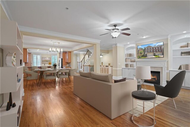 living room with ceiling fan with notable chandelier, light hardwood / wood-style floors, a fireplace, and ornamental molding