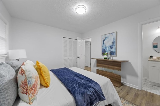 bedroom with a closet, ensuite bath, a textured ceiling, and light hardwood / wood-style flooring