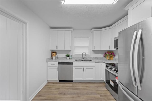 kitchen with appliances with stainless steel finishes, sink, white cabinets, a textured ceiling, and light hardwood / wood-style flooring