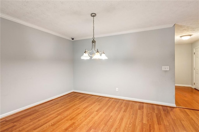 spare room with ornamental molding, wood finished floors, baseboards, a textured ceiling, and a chandelier