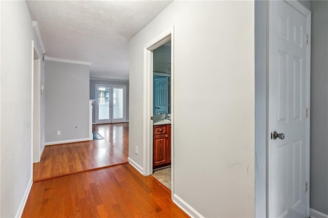 corridor featuring light wood-style flooring, baseboards, a textured ceiling, and ornamental molding