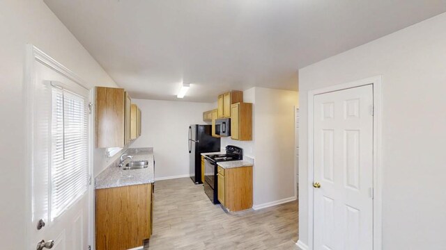 kitchen featuring light wood finished floors, stainless steel microwave, black range with electric stovetop, baseboards, and a sink