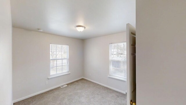 unfurnished room featuring baseboards, plenty of natural light, light carpet, and visible vents