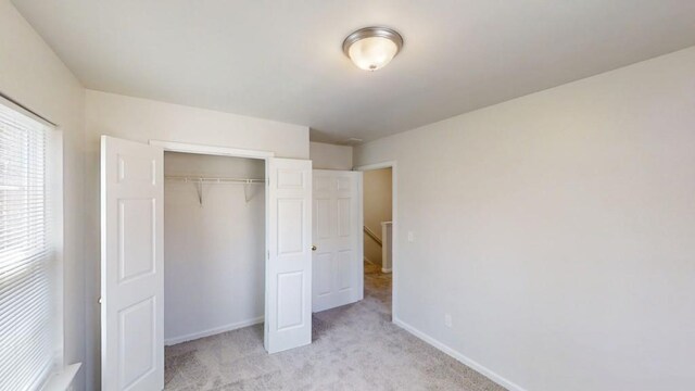 unfurnished bedroom featuring light carpet, a closet, and baseboards