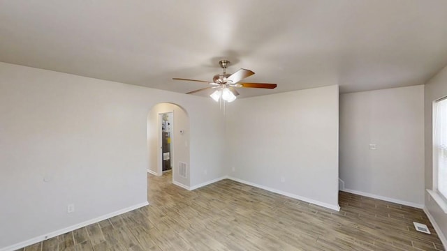 unfurnished room with visible vents, baseboards, wood finished floors, arched walkways, and a ceiling fan