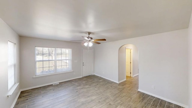 spare room with arched walkways, ceiling fan, baseboards, and wood finished floors