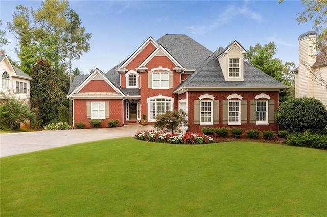 view of front facade with roof with shingles, a front lawn, and brick siding