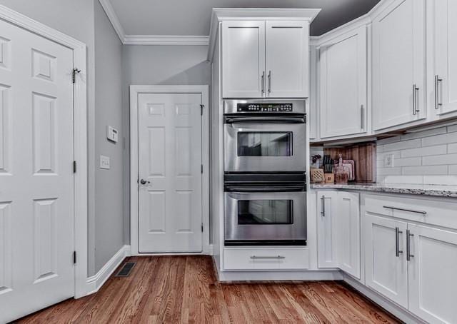 kitchen featuring ornamental molding, white cabinetry, wood finished floors, backsplash, and stainless steel double oven