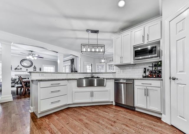 kitchen with ceiling fan, a peninsula, appliances with stainless steel finishes, wood finished floors, and a sink