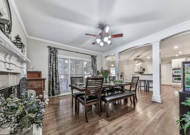 living area with ornamental molding, decorative columns, stairs, and ceiling fan with notable chandelier
